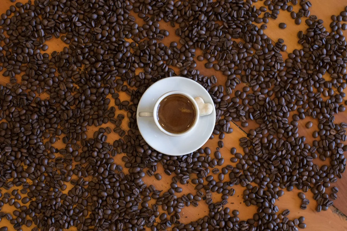 Roasted coffee beans scattered beside two white coffee cups on a wooden table