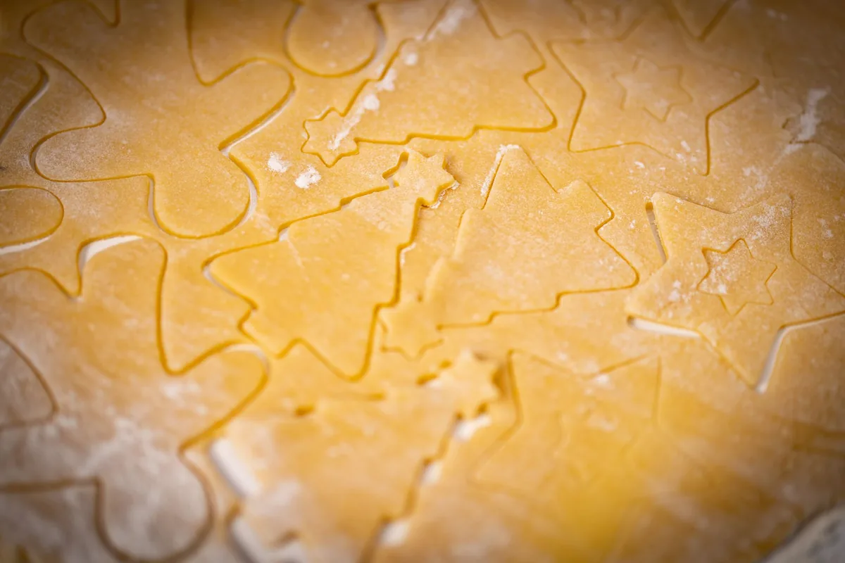 Rolled cookie dough with star and round shapes cut out on a baking surface