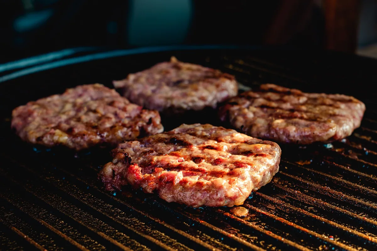 Round burger patties searing on a metal grill grate with visible grill marks