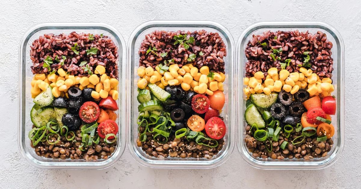 Rows of clear glass food containers filled with rice, vegetables and chicken on a bright kitchen counter