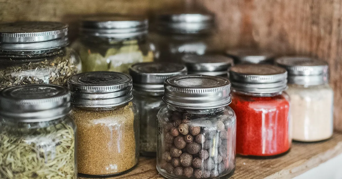 Rows of glass spice jars filled with colourful ground spices on a light kitchen shelf