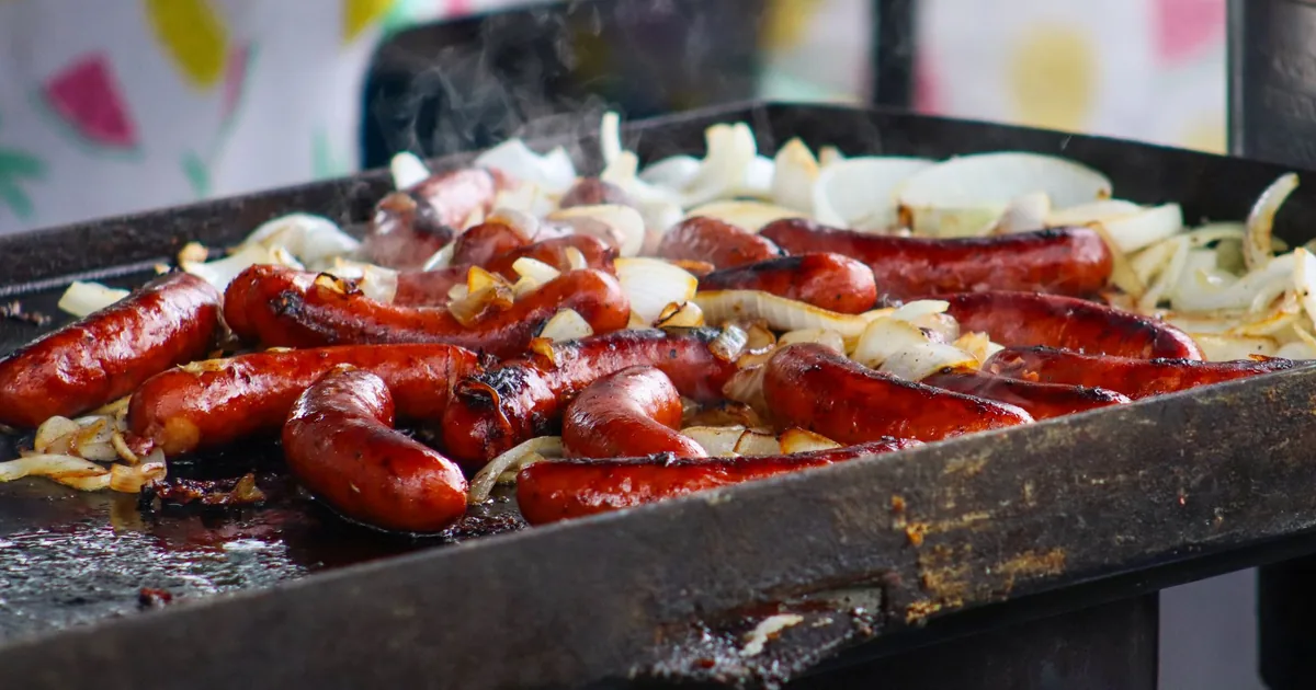 Sausages and sliced onions cooking on a flat-top griddle