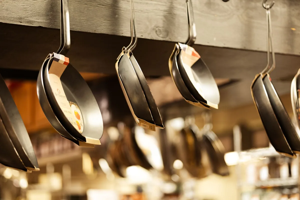 Several frying pans of different sizes hanging on a rail above a kitchen counter