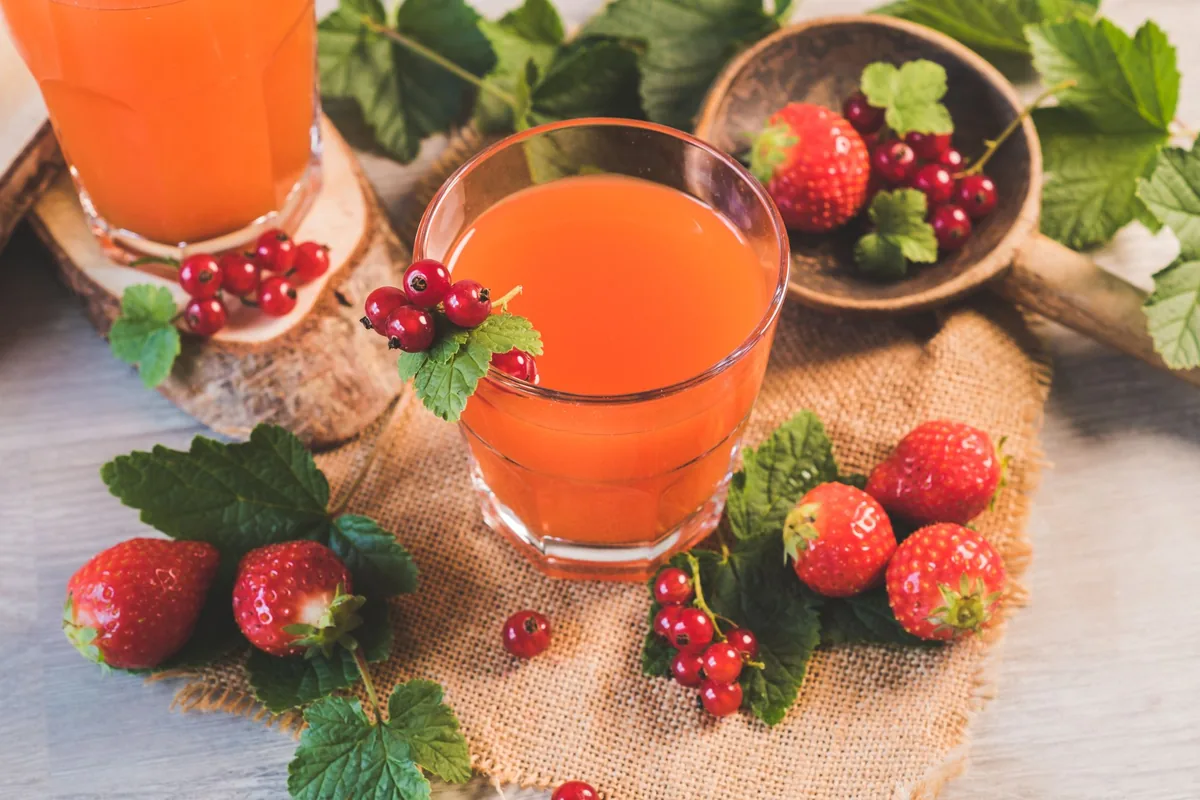 Several glasses of orange, red and green fruit juice lined up on a sunlit table