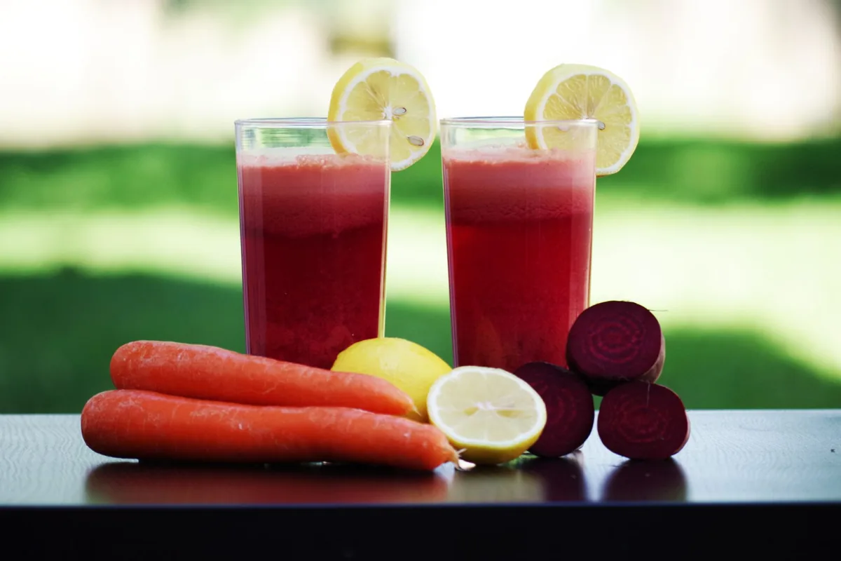 Several glasses of orange, red and green juice lined up on a white surface in daylight