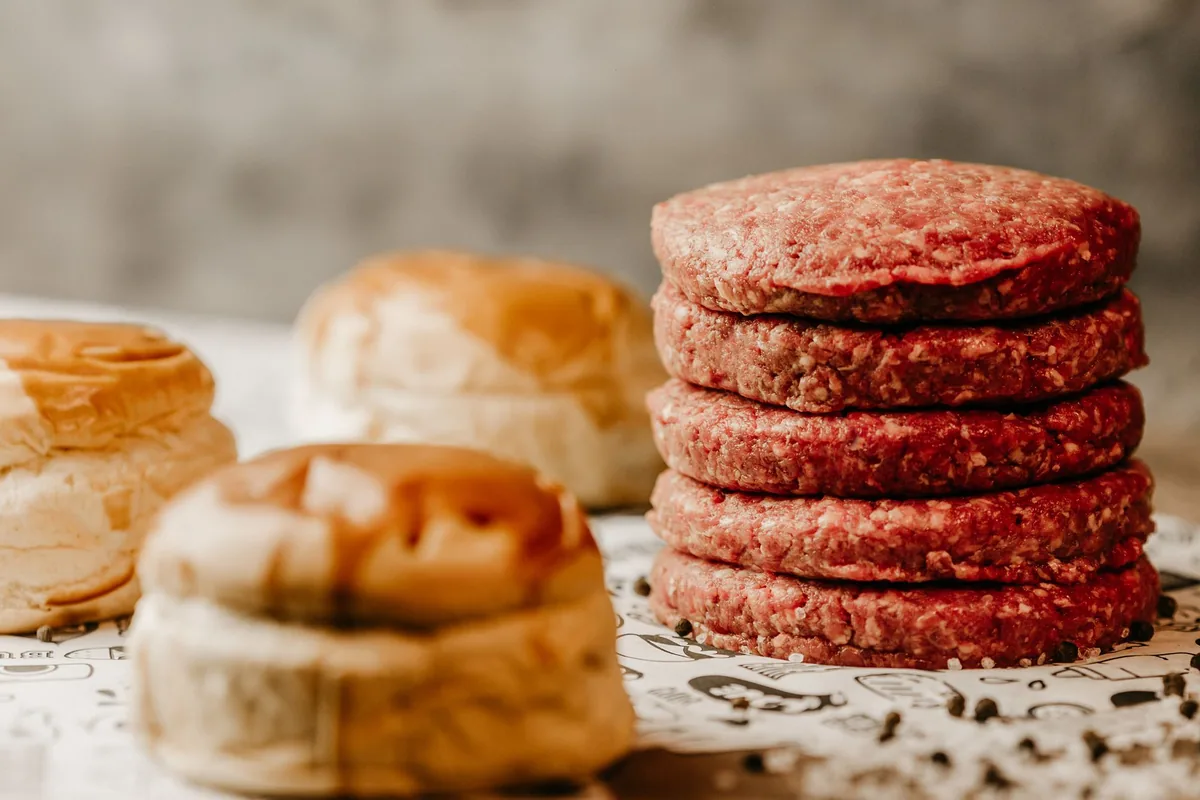 Several round raw burger patties on parchment paper on a kitchen counter