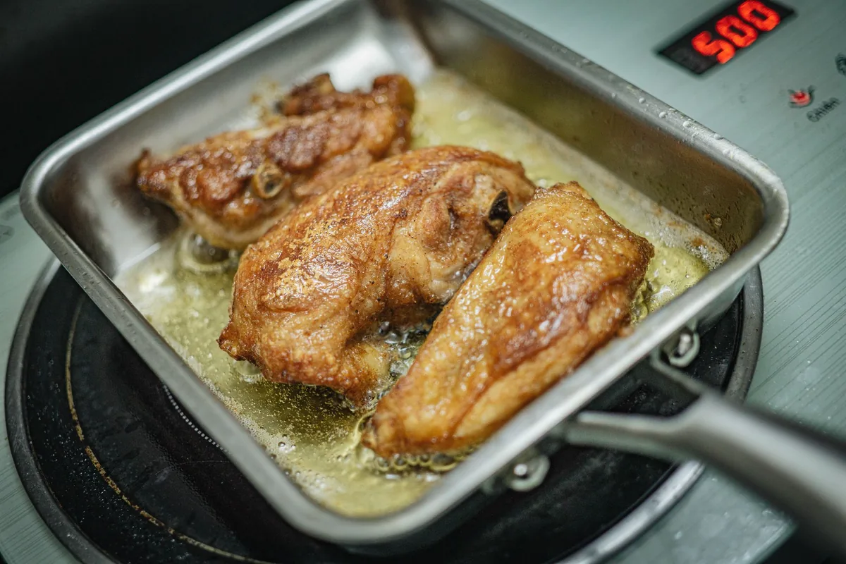 Browned chicken pieces in a square stainless pan on an induction hob