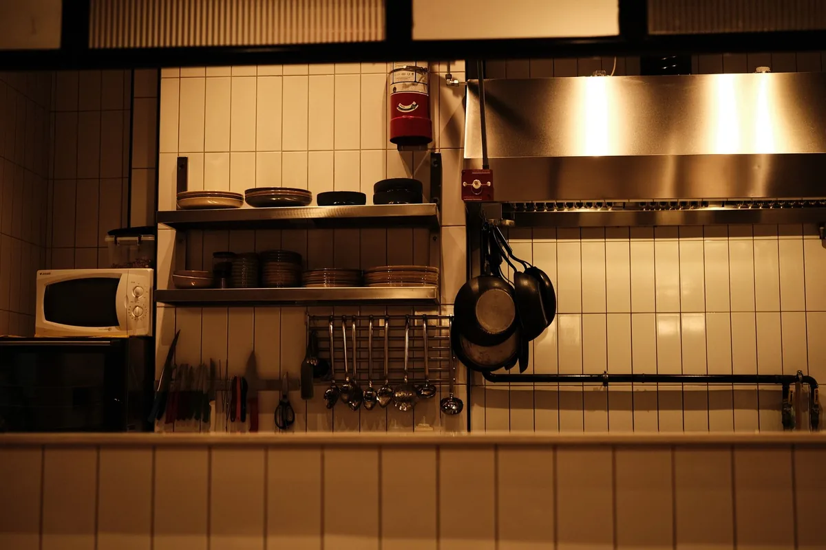 Several stainless steel frying pans of different sizes hanging from a rail in a bright kitchen