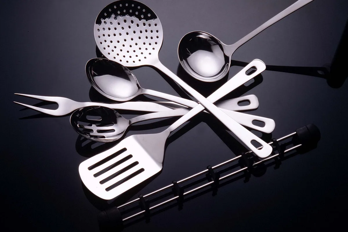 Several stainless steel spatulas and turners laid side by side on a wooden counter