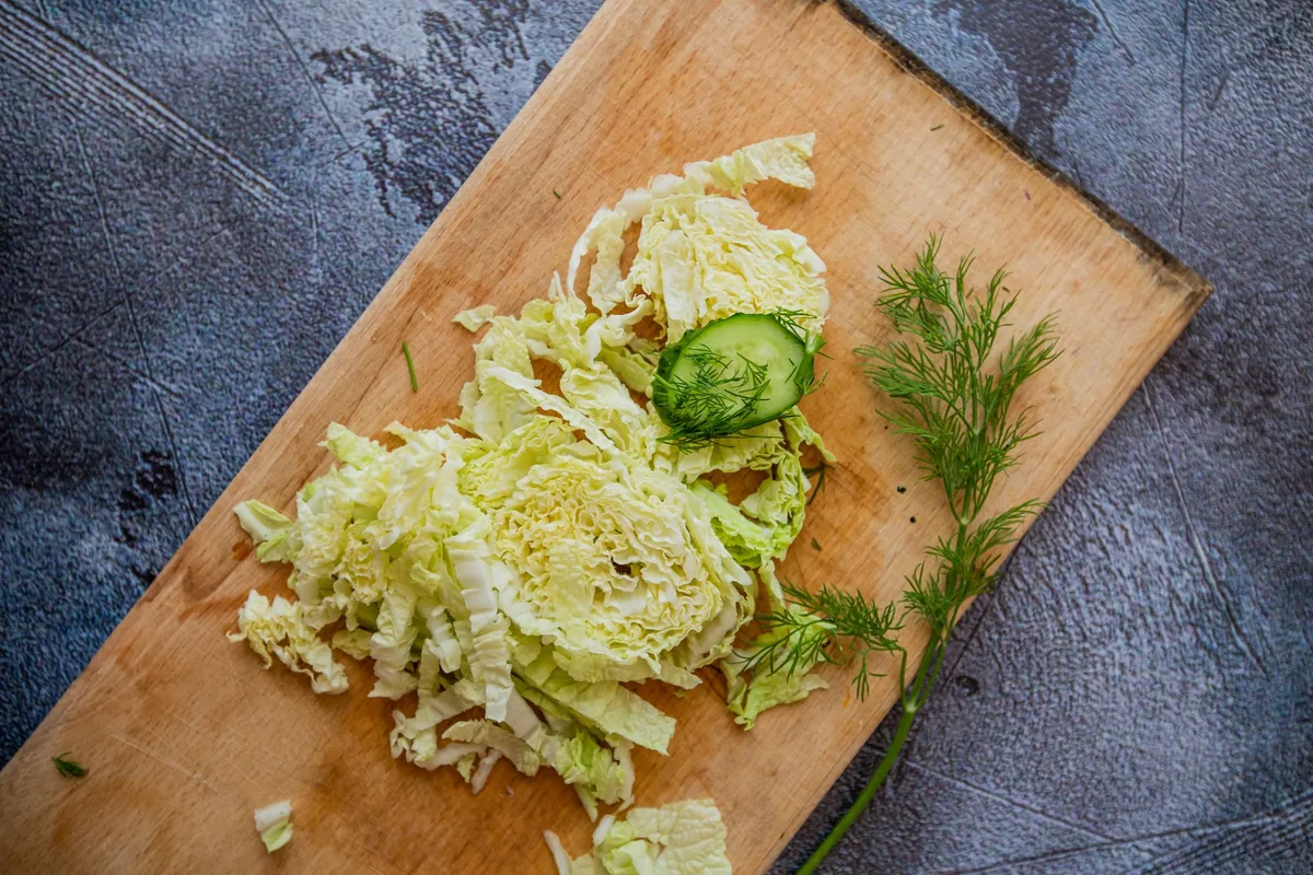 Shredded cabbage and thin, even cucumber slices on a white cutting board