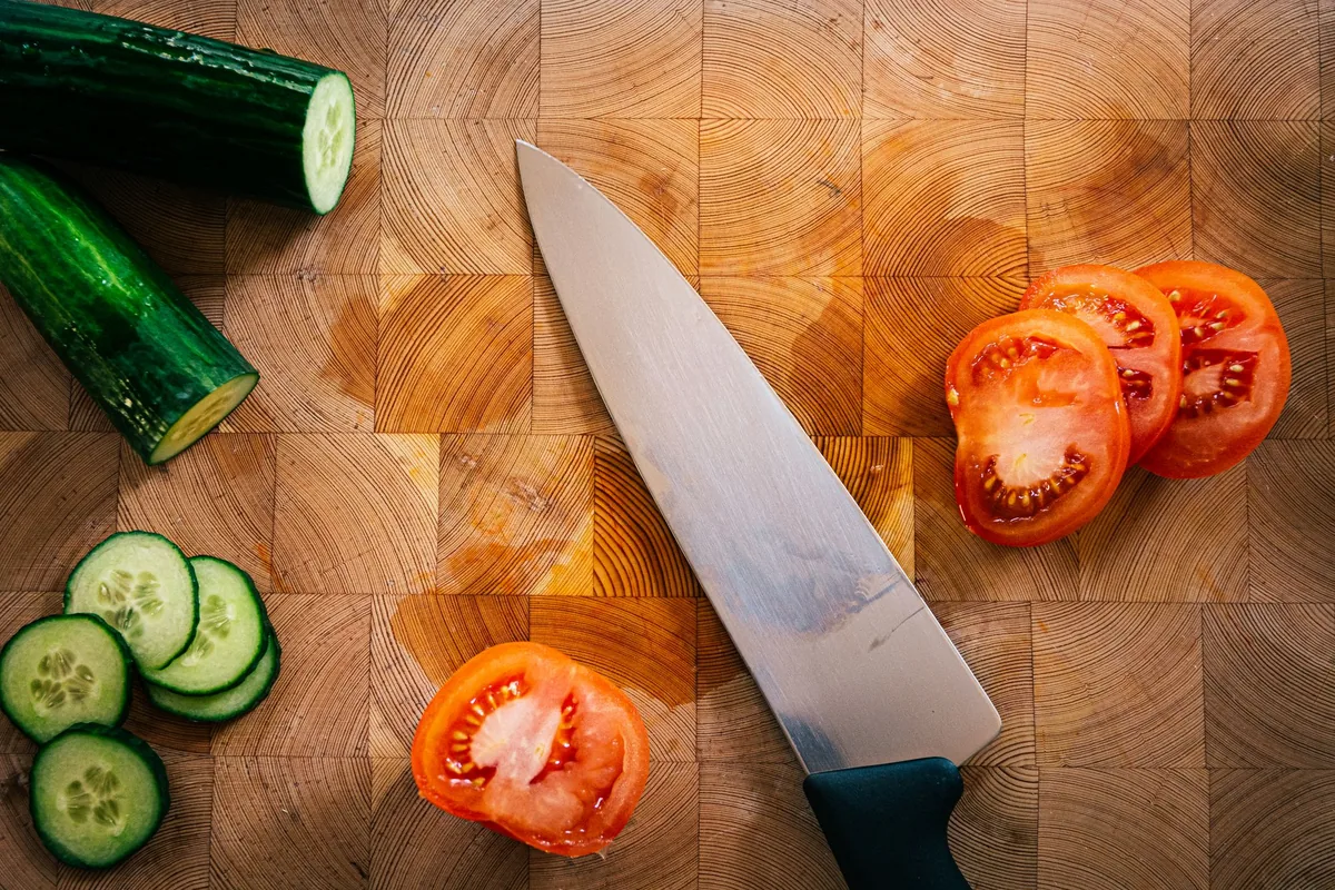 Sliced cucumber and tomatoes beside a knife on a wooden board