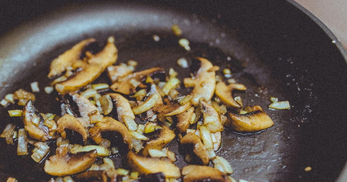 Sliced mushrooms cooking in a dark nonstick pan