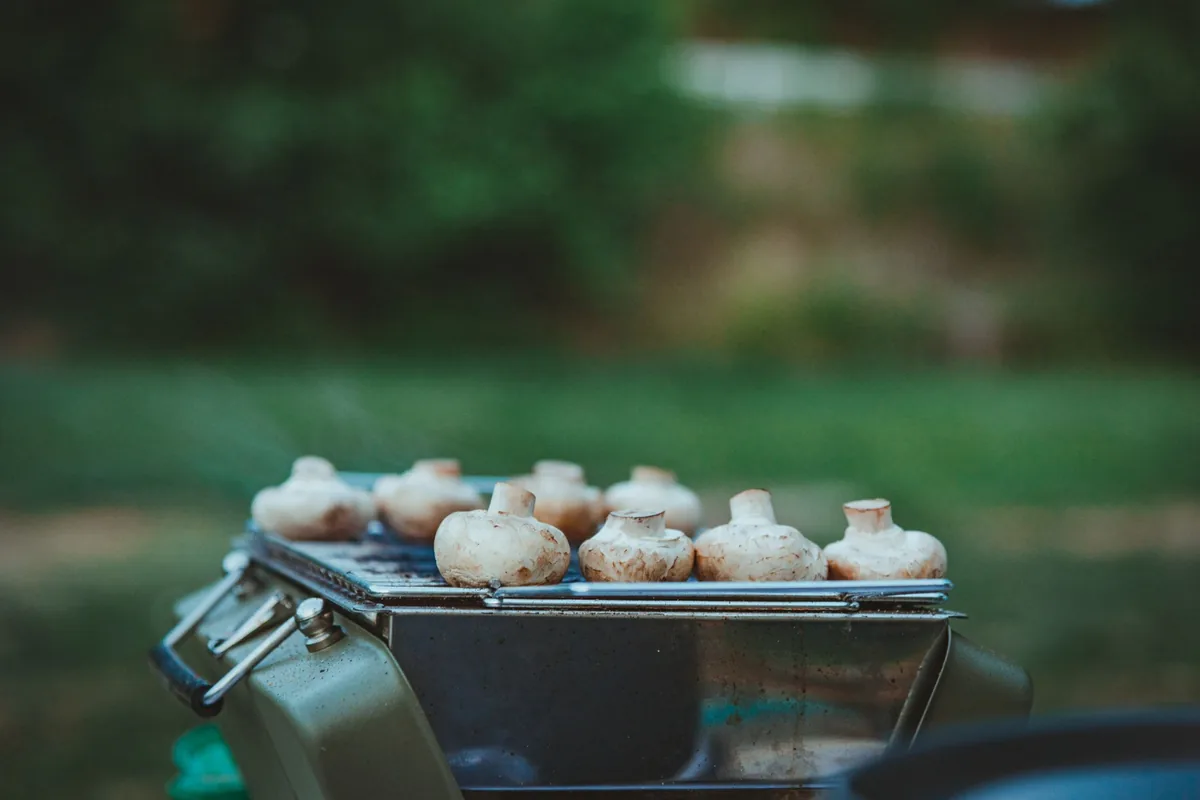 Mushrooms cooking on the grate of a small portable grill outdoors