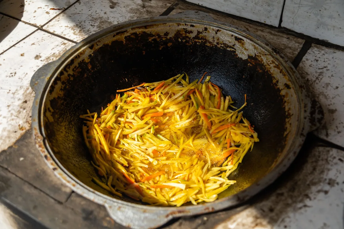 Sliced peppers and onions sauteing in a dark skillet on a burner