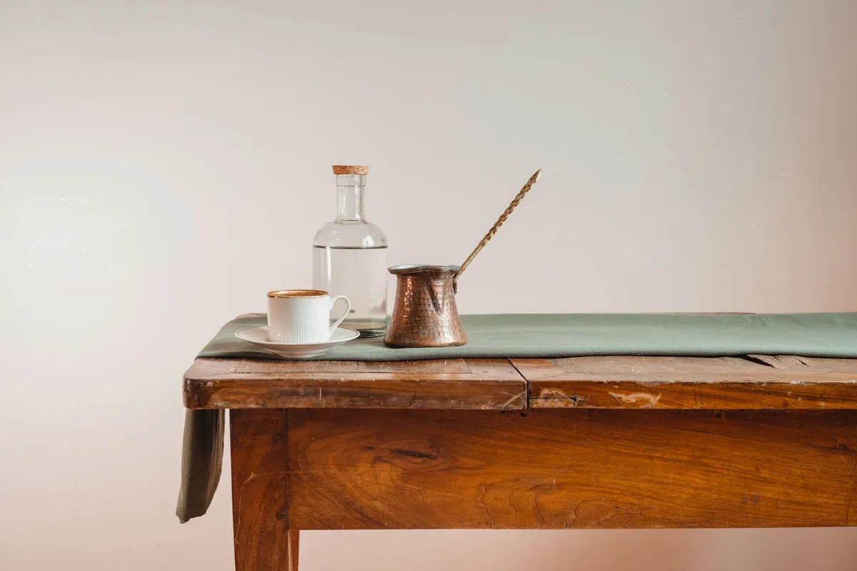 A small cup, a copper coffee pot and a water bottle on a side table