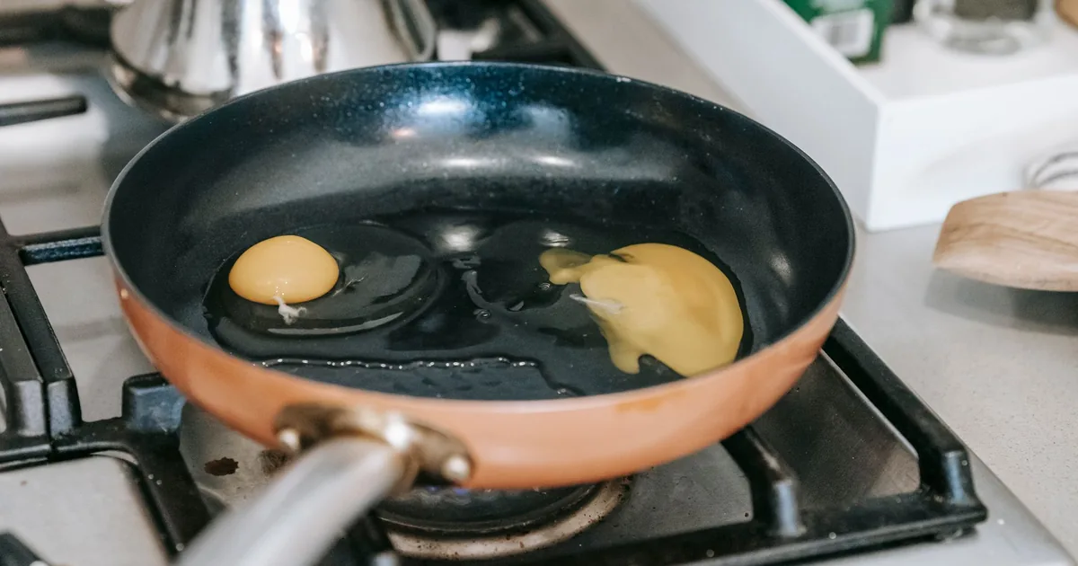 Small pancakes cooking in a copper-coloured nonstick pan on a gas stove