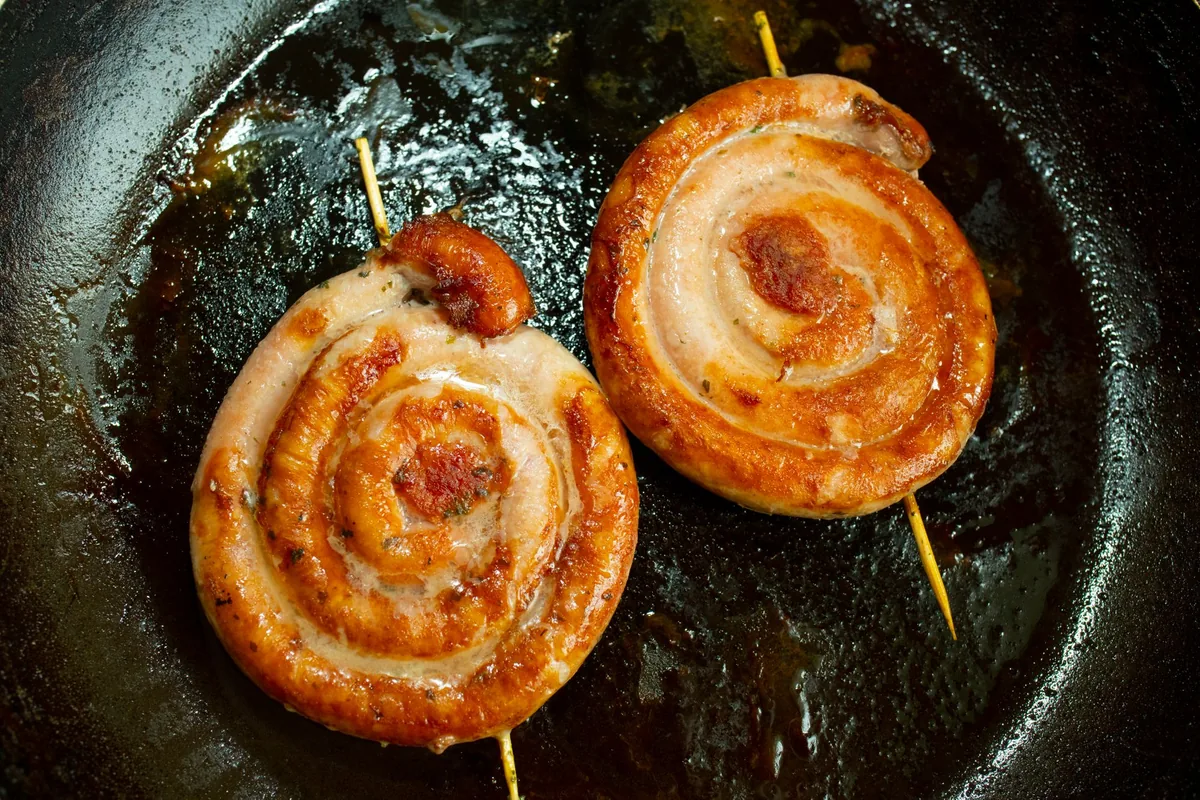 Spiral sausages browning in a dark pan