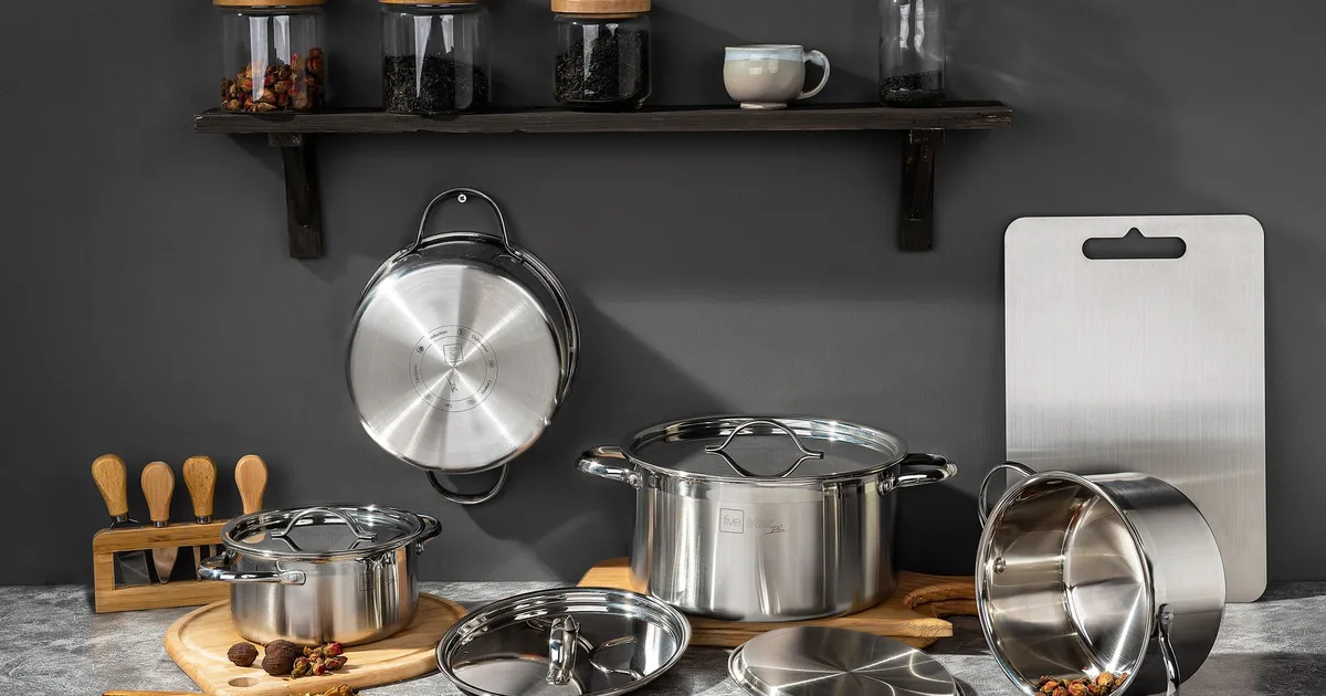 Stainless pots and pans on a grey counter below a shelf