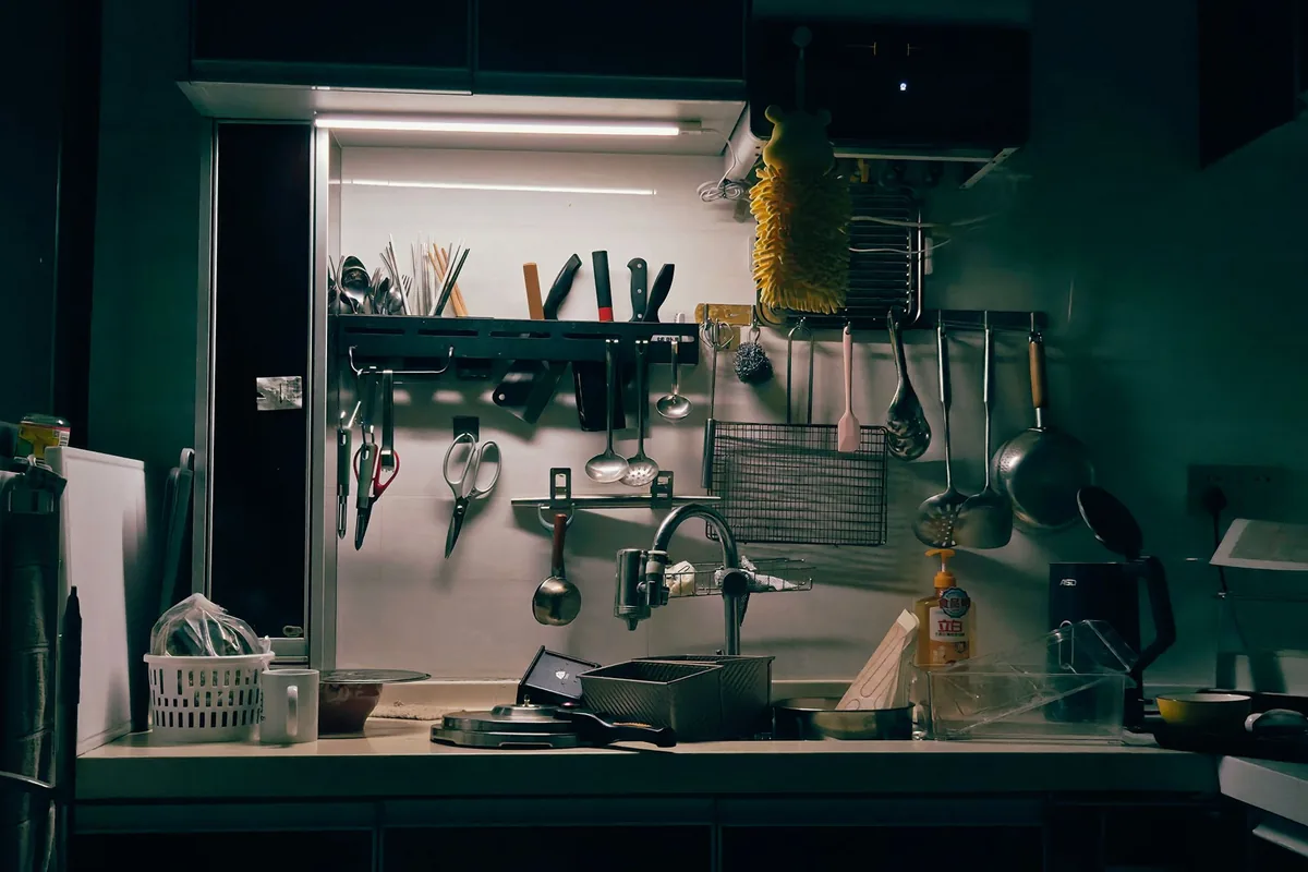 Stainless steel kitchen utensils hanging from a wall rail above a worktop