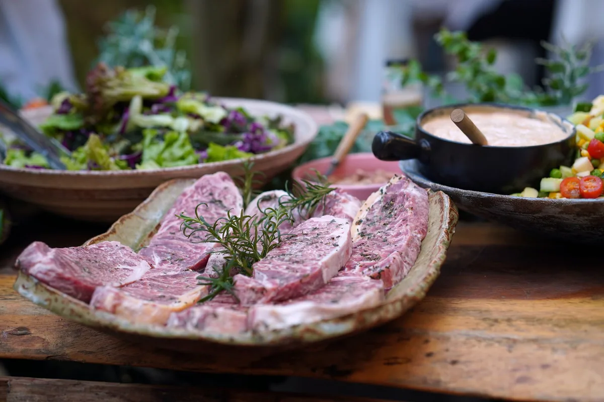 Steaks resting in a glass dish of marinade with herbs and garlic