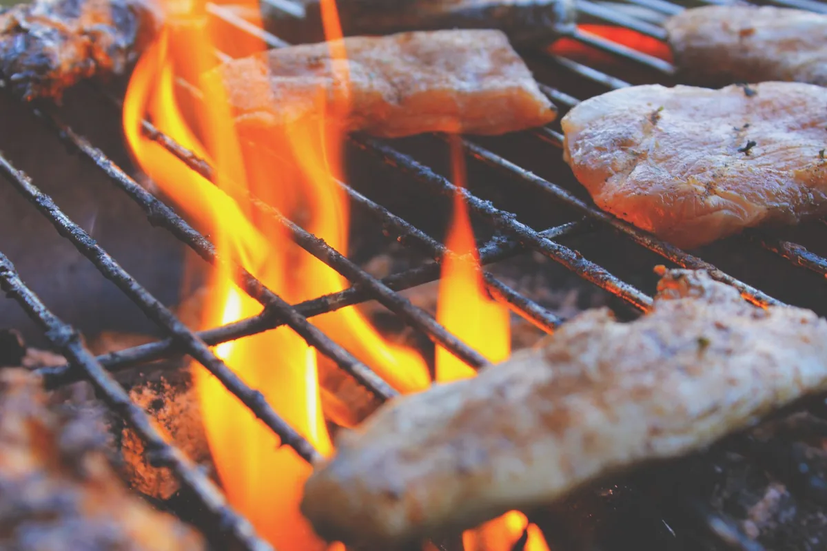 Steaks with dark sear marks on cast iron grill grates over gas flames