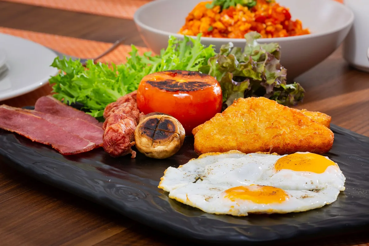 A breakfast plate with fried eggs, tomato and hash brown