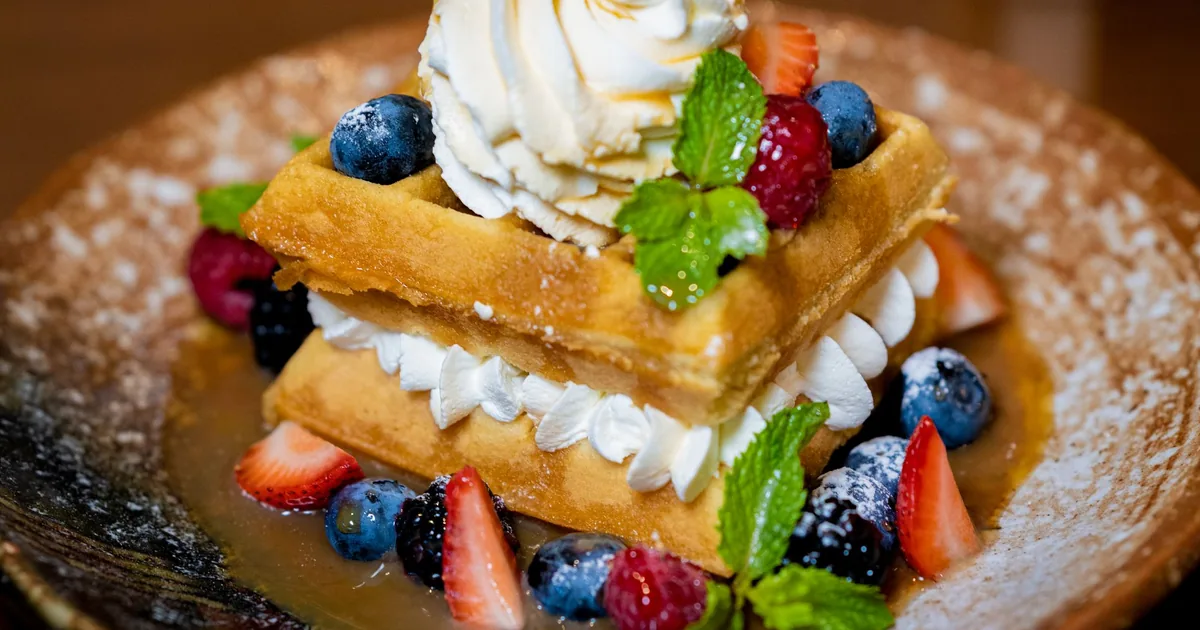 Thick golden Belgian waffles with deep square pockets topped with fresh berries on a white plate