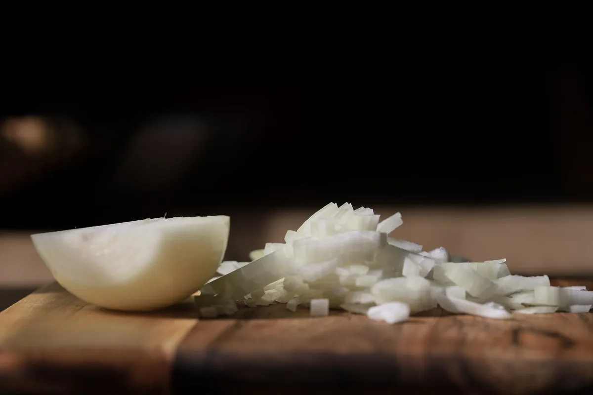 Thin rings of sliced white onion spread across a wooden cutting board