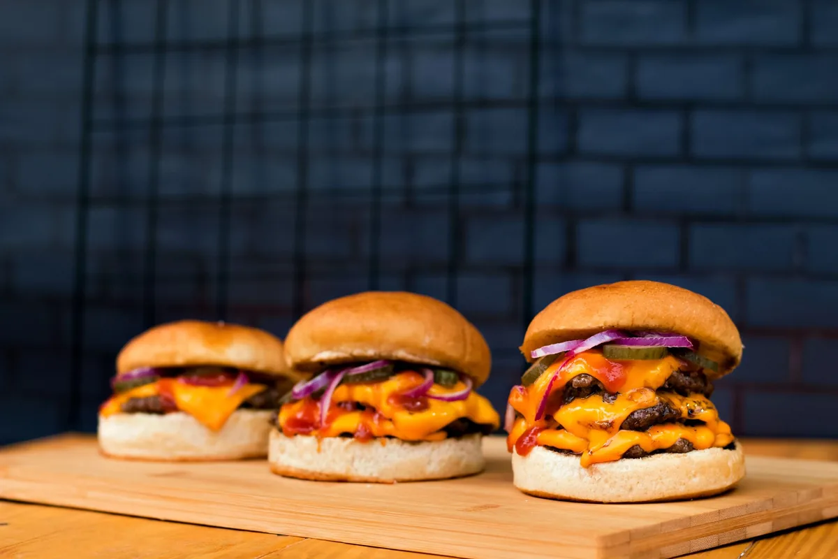 Three cheeseburgers lined up on a wooden board