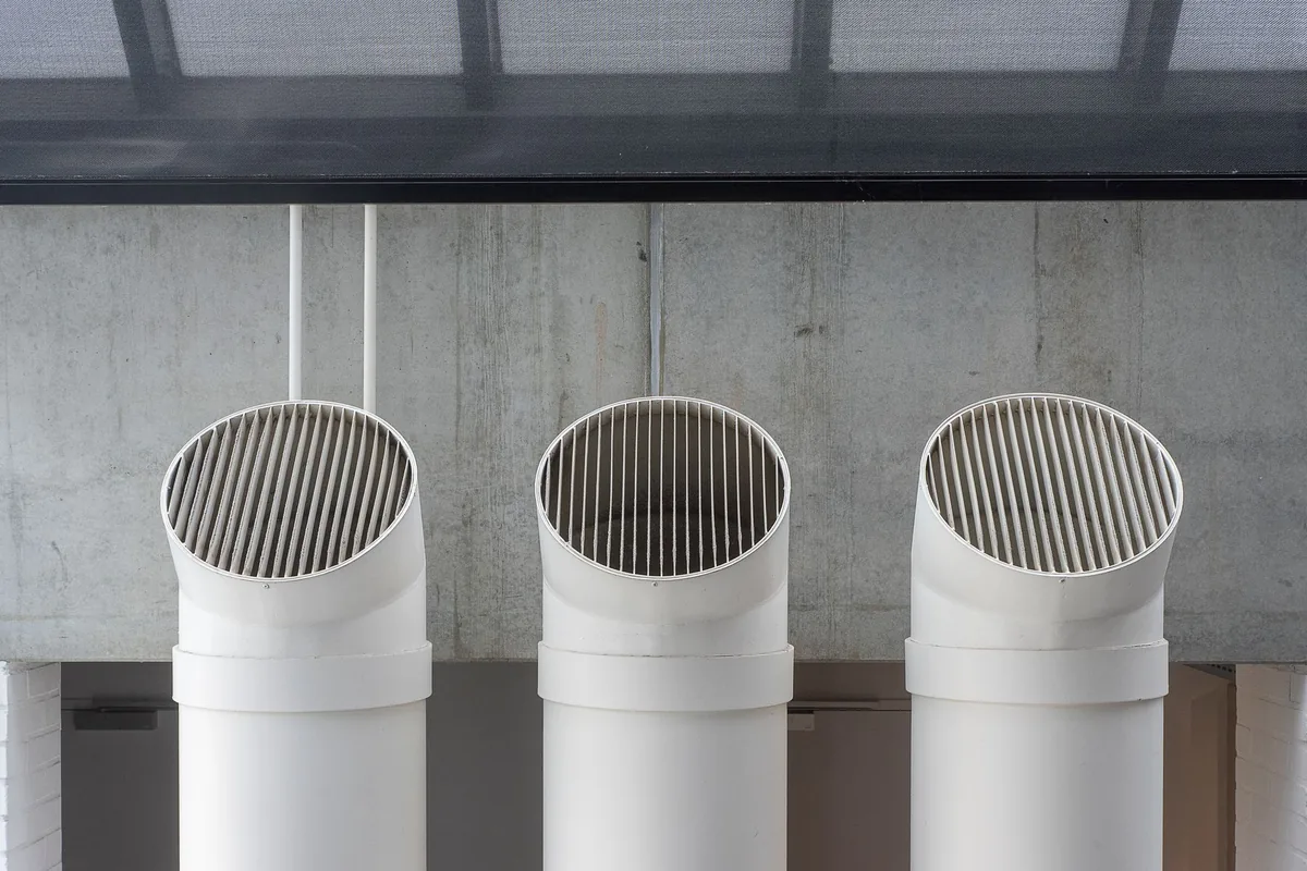 Three round white ducts mounted against a concrete wall