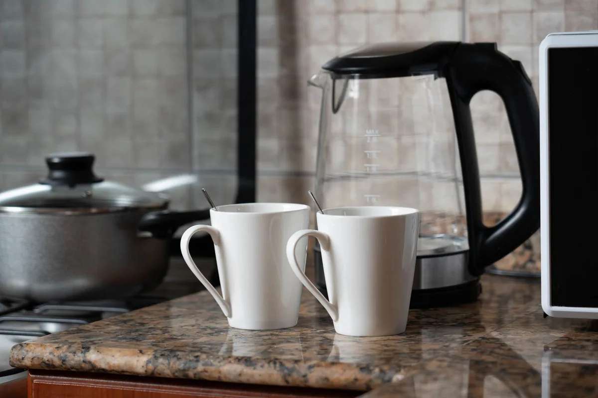 Two white mugs beside an electric kettle on a kitchen counter