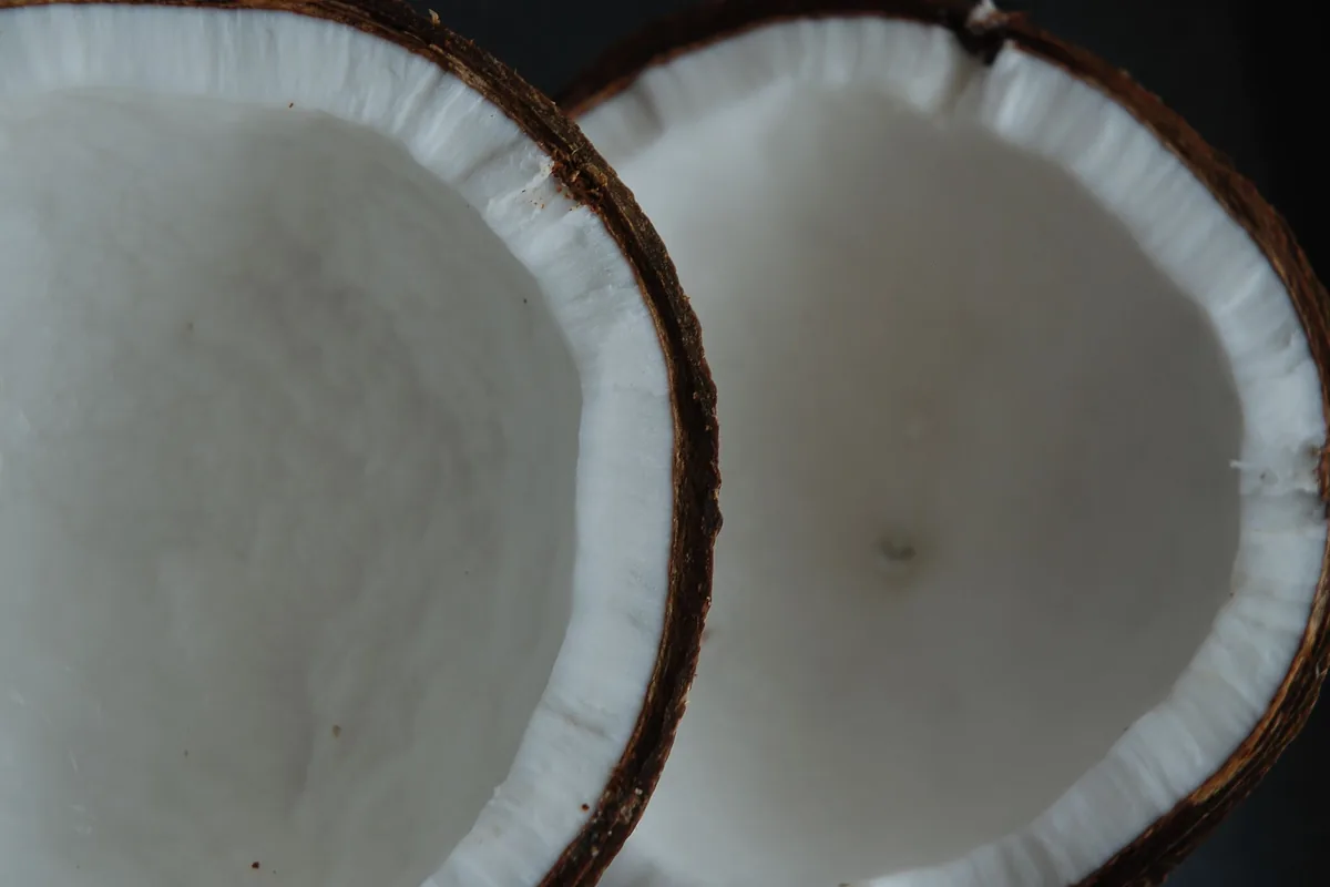 Two halves of a fresh coconut showing white flesh on a pale wooden surface