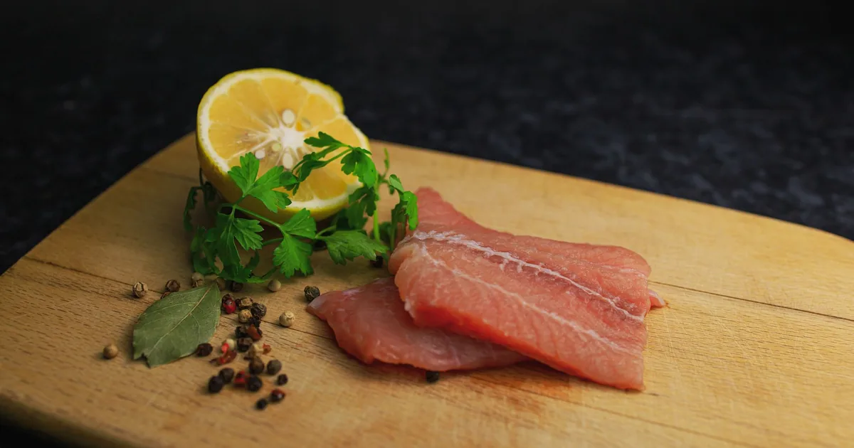 Two pink fish fillets laid side by side on a light wooden cutting board in daylight