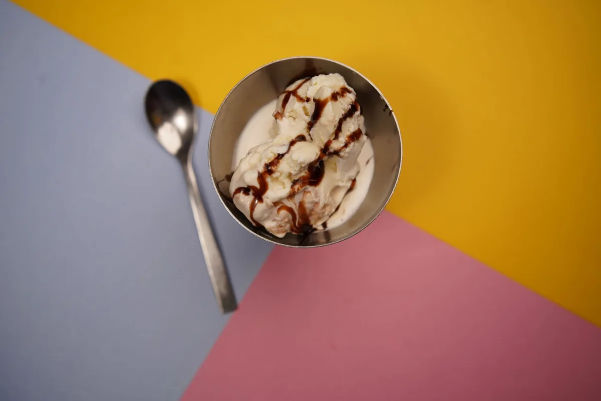 Two scoops of vanilla ice cream in a white ceramic bowl on a wooden table