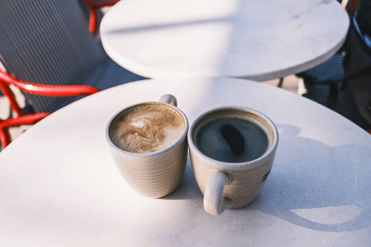 Two white mugs of black coffee side by side on a wooden table