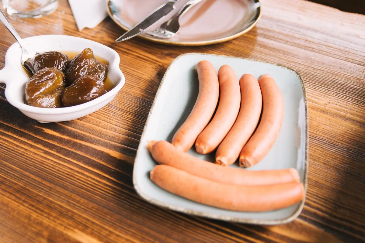 Uncooked sausages on a white tray on a wooden table