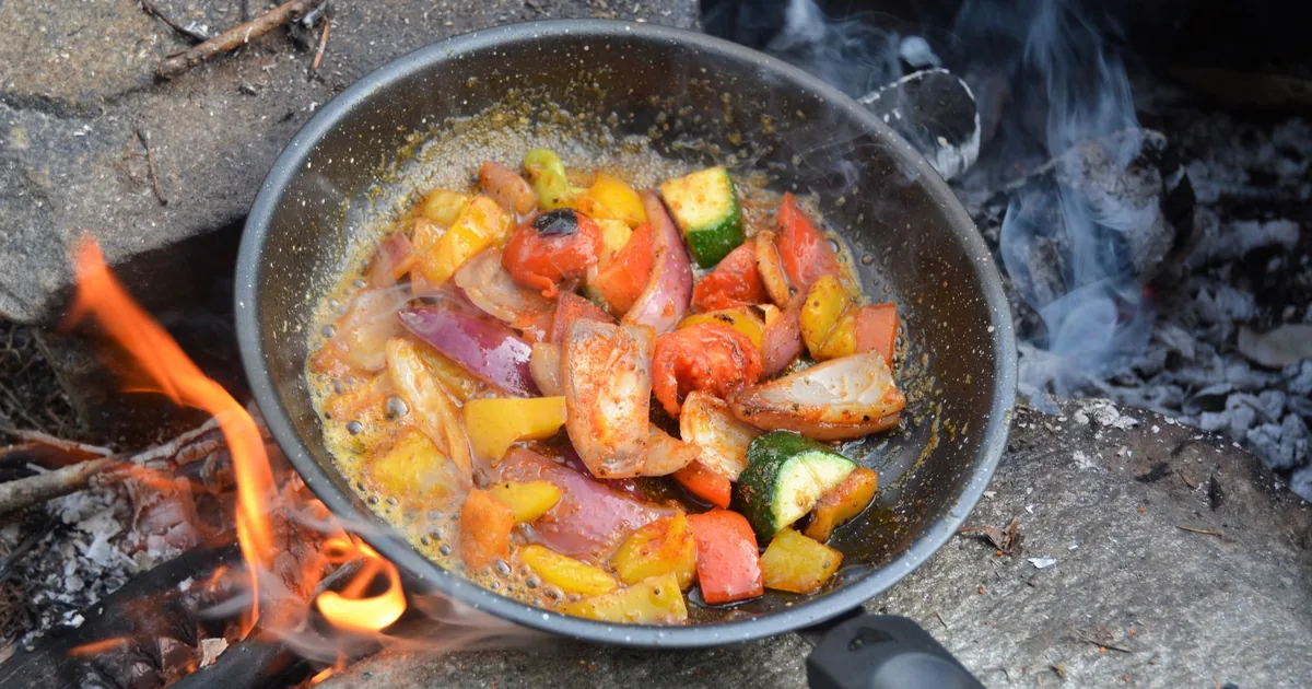 Vegetables cooking in a steel pan over a campfire
