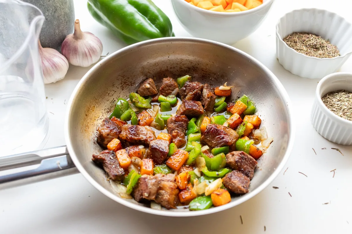 Vegetables cooking in a straight-sided stainless steel pan on a gas burner