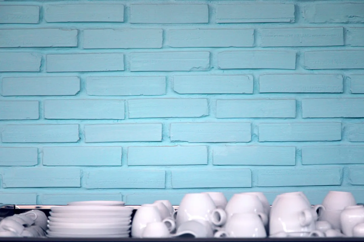 White cups and bowls lined on a shelf against blue brick