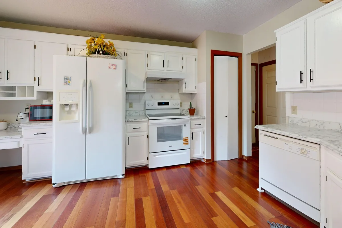 White kitchen base cabinets above a light wooden floor with a narrow gap at one end