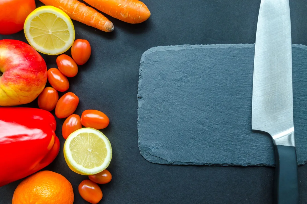 Whole red apples and bright orange carrots arranged on a wooden cutting board