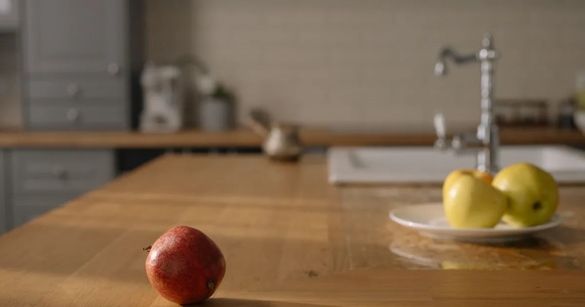 Whole red apples and oranges piled on a bright kitchen worktop beside a glass of juice