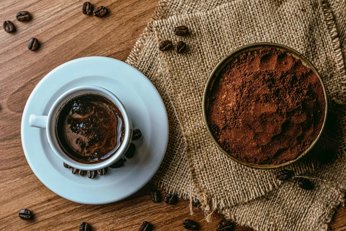 Whole roasted coffee beans beside a small pile of ground coffee on a wooden table