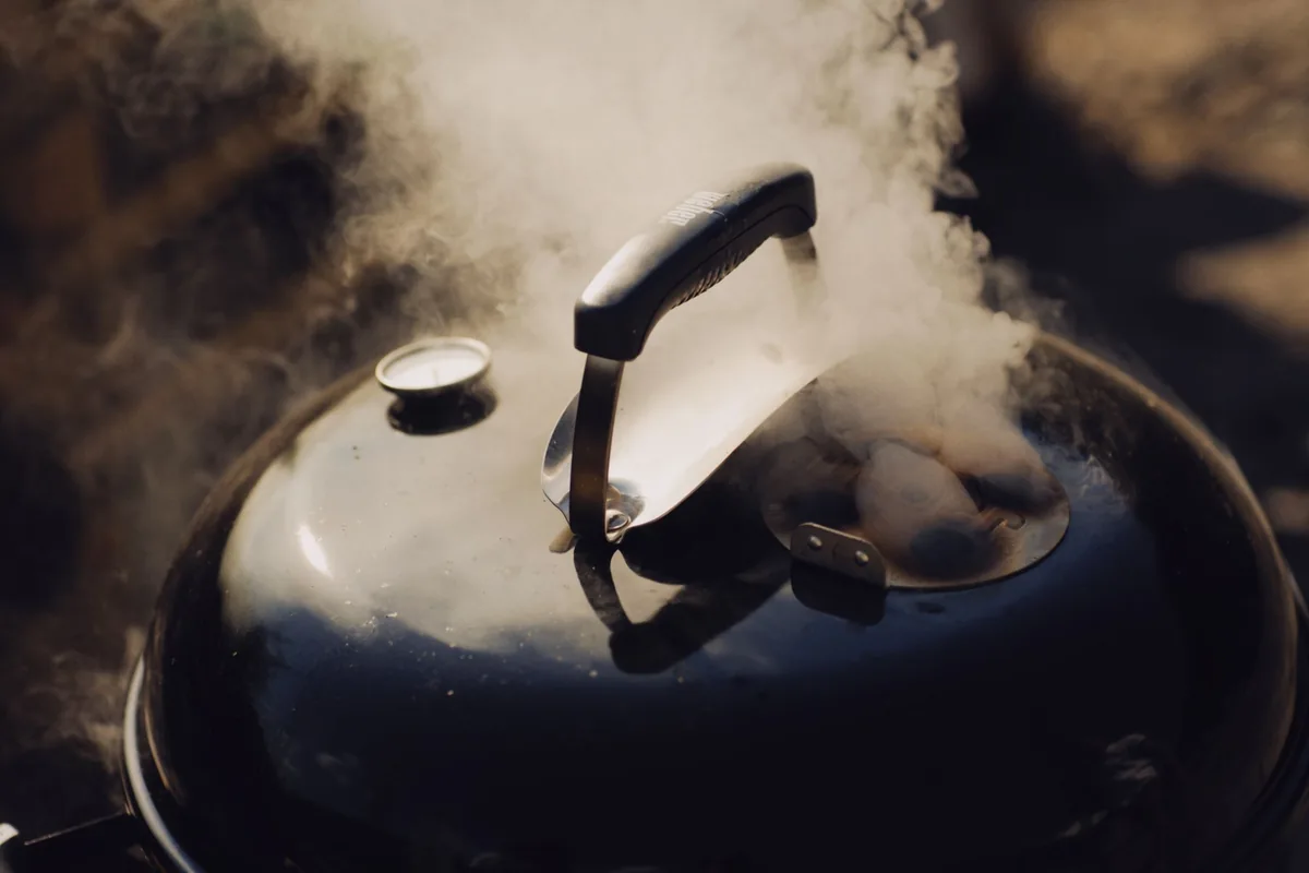 Steam rising from under the lid of a kettle grill